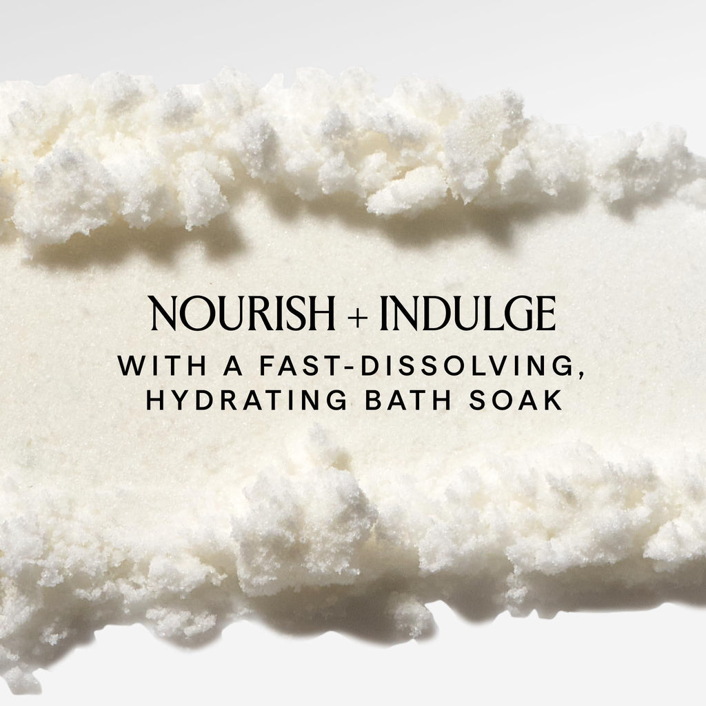 Herbivore Coconut Milk Bath Soak in a clear glass jar with a scoop, surrounded by coconut shells and dried botanicals.